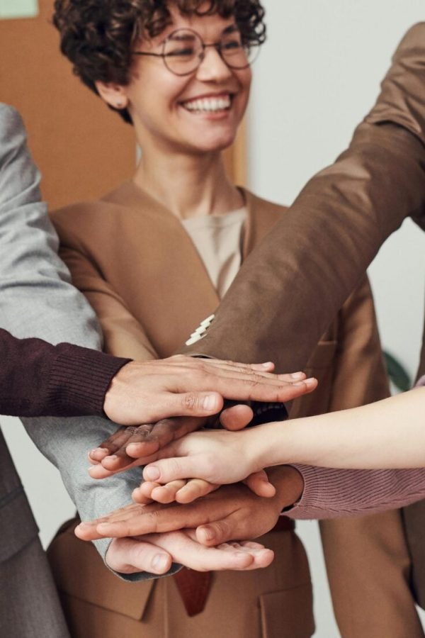 A group of happy, diverse colleagues celebrating teamwork and cooperation with a group high five indoors.